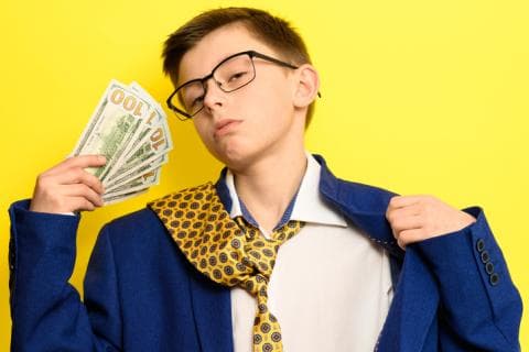 A child in an oversized suit jacket and yellow tie displays a wad of cash