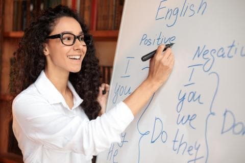 A teacher writes English phrases on a whiteboard