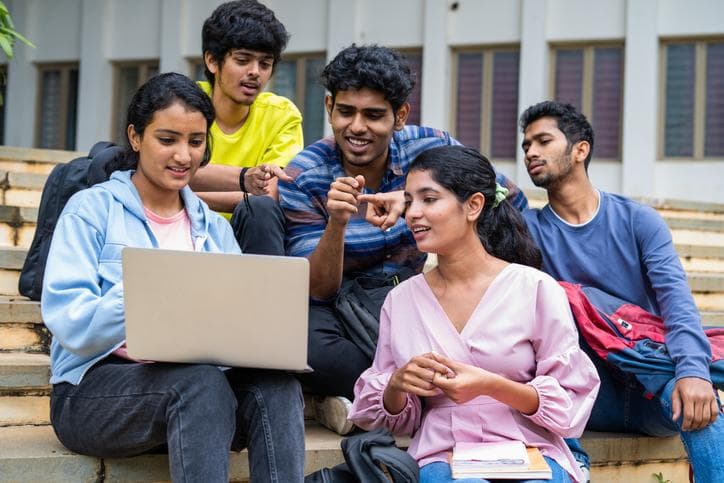 Group of happy students checking results on laptop while sitting on college campus